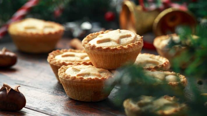 British Christmas mince pies with decoration, gifts, green tree branch on wooden rustic table.